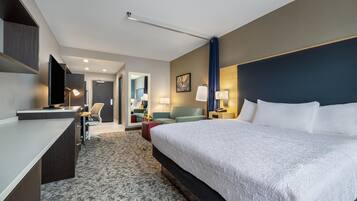 A hotel room with a large bed, a desk, a chair, a sofa, and a TV.