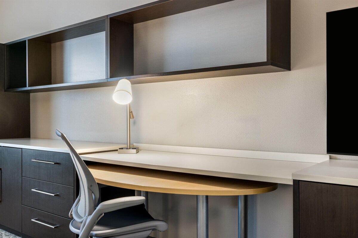 A modern office desk with a lamp, a chair, and a built-in shelf.