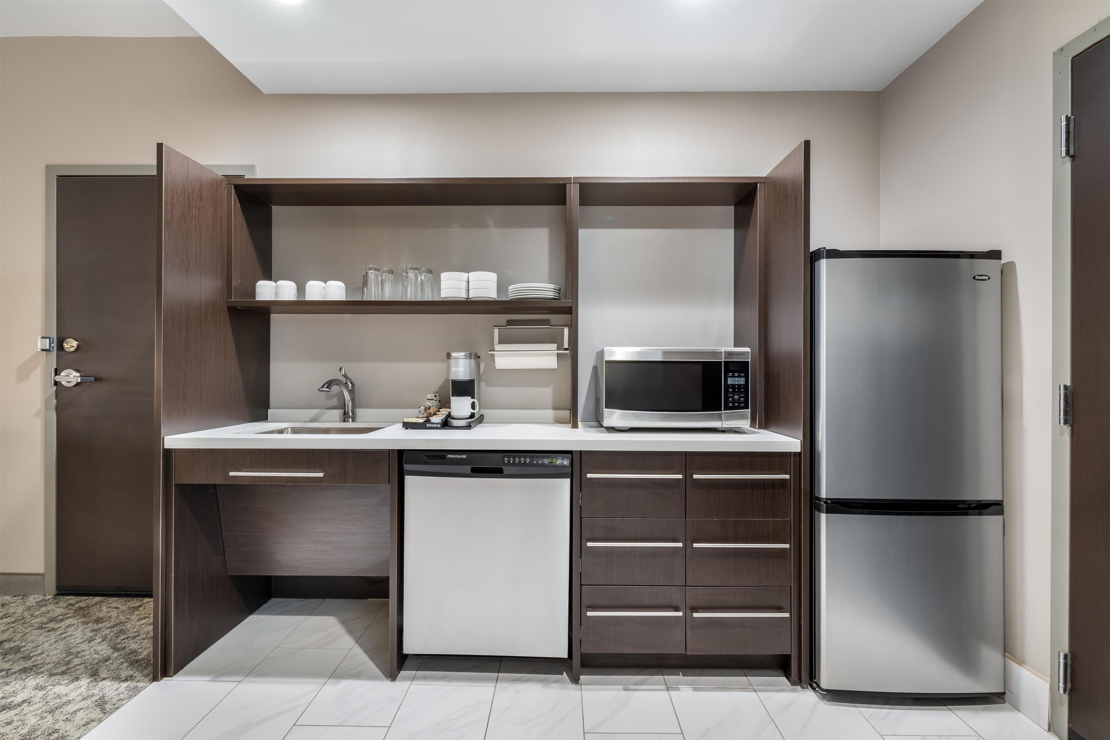 A compact kitchen with a built-in dishwasher, a microwave, and a stainless steel refrigerator.