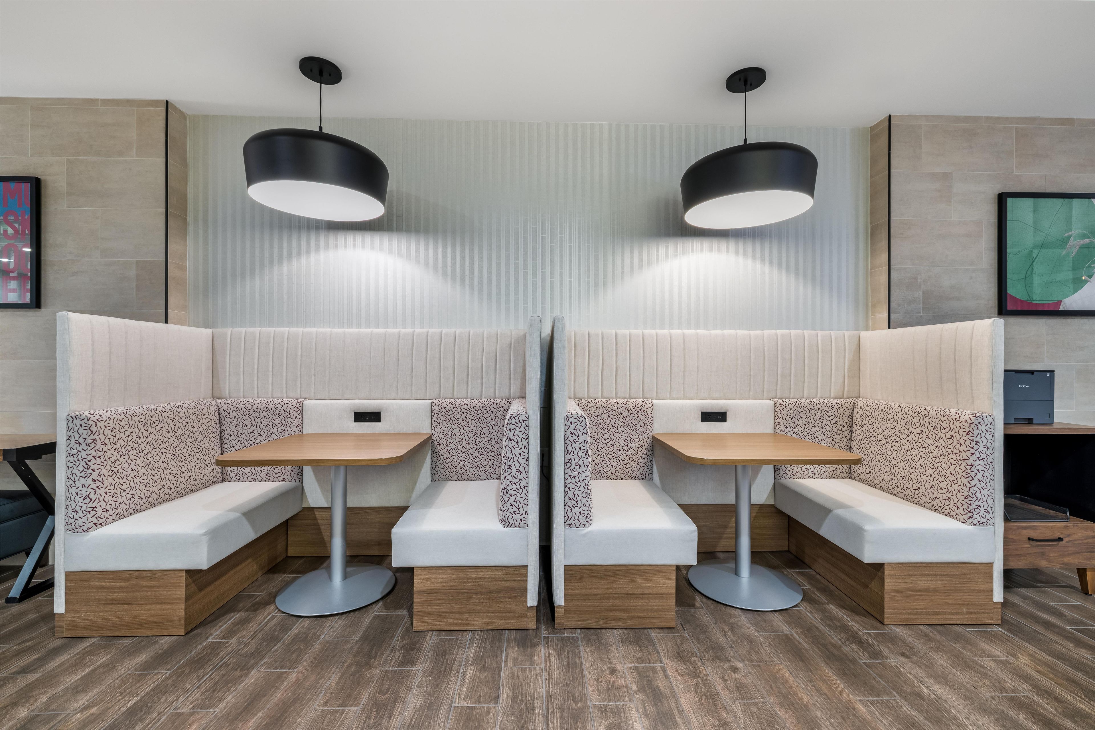 Un área de estar moderna con dos mesas, bancos, iluminación colgante y un muro con diseño.
