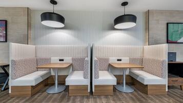 Un área de estar moderna con dos mesas, bancos, iluminación colgante y un muro con diseño.