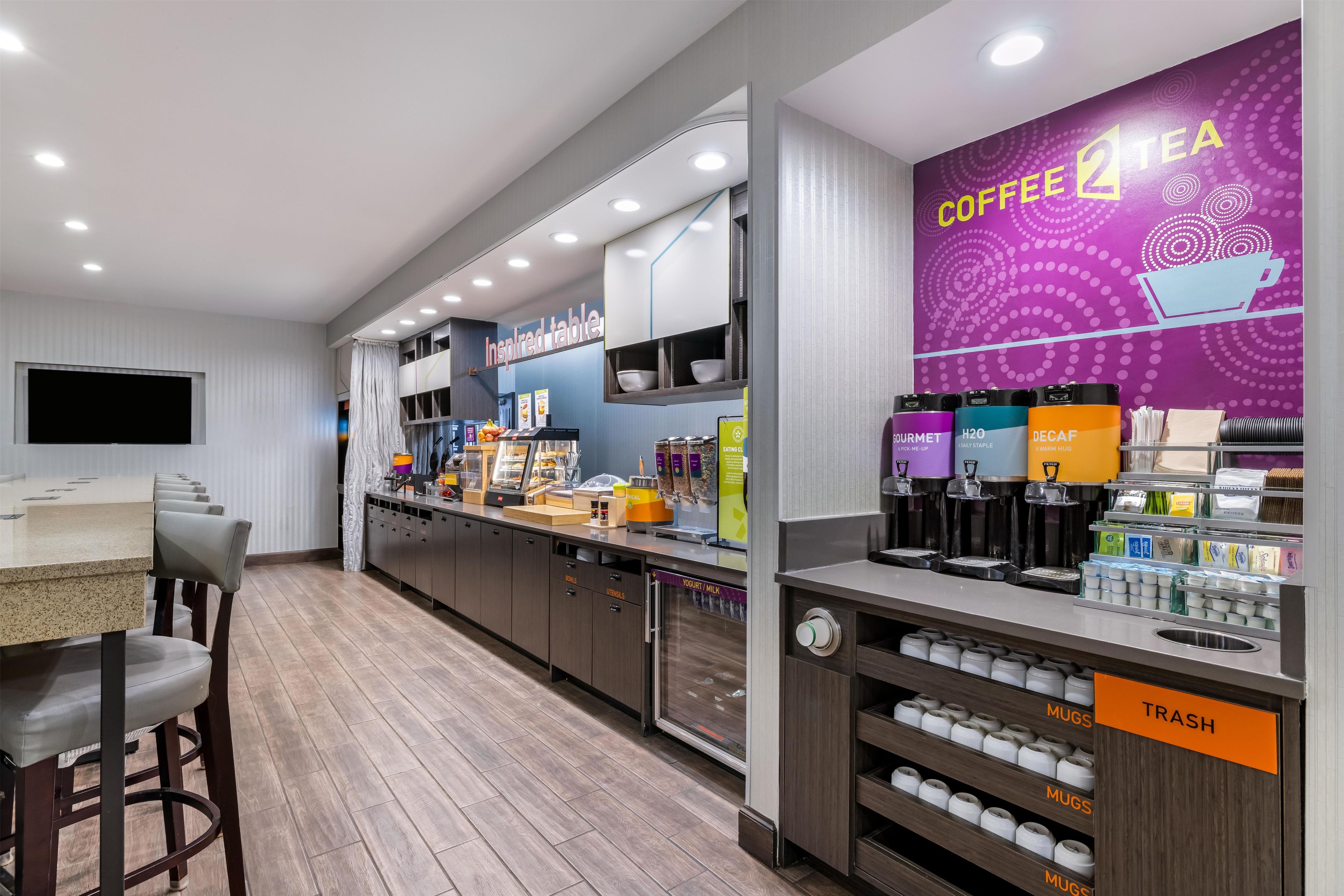 Una cafetería moderna con mostrador, zona de mesas y un mural con temática de café.
