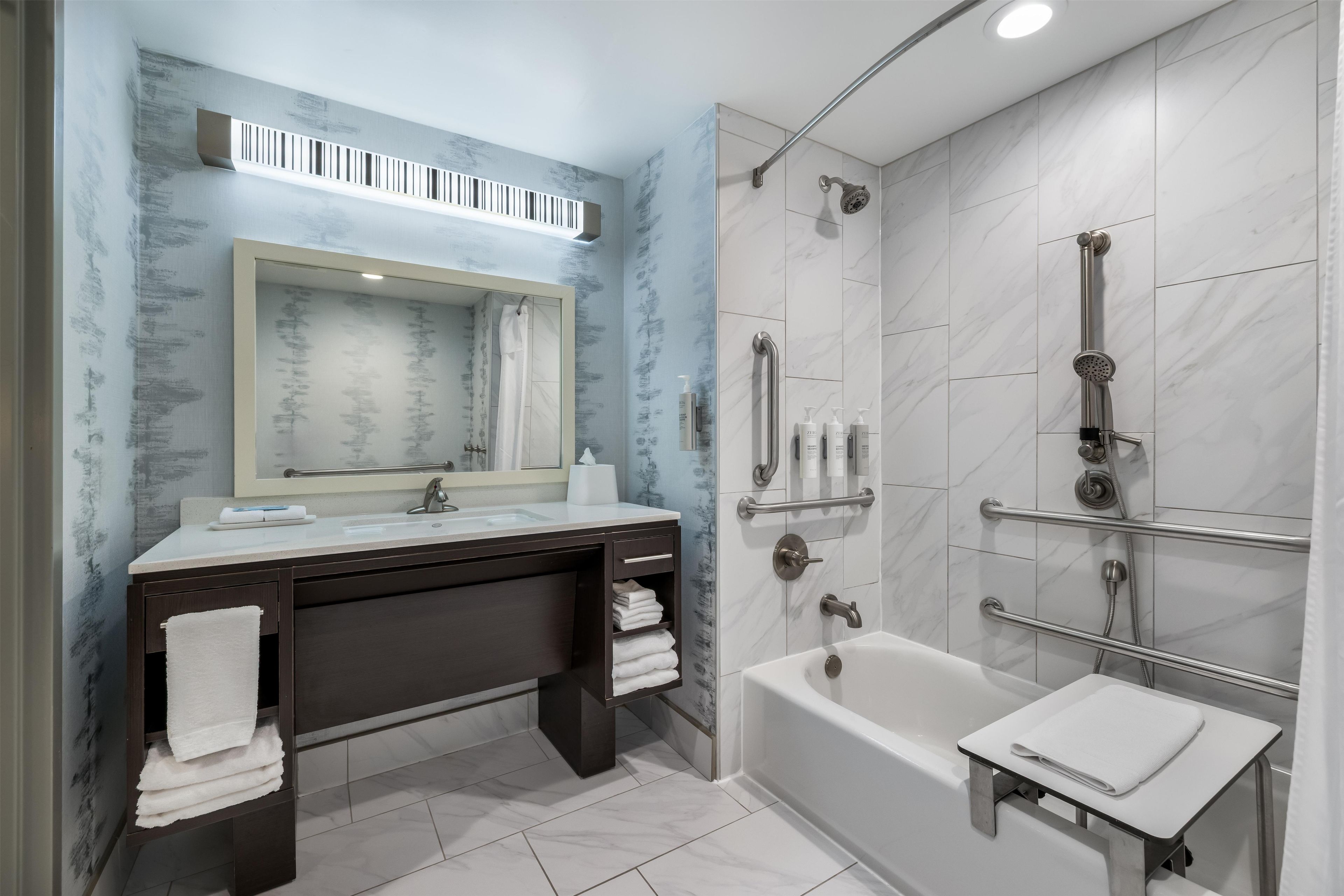 A modern bathroom with a bathtub, a shower with grab bars, a vanity with a mirror, and a towel rack.