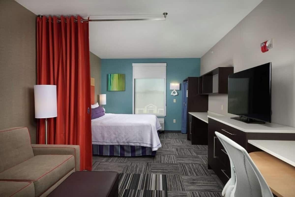 Habitació d'hotel amb un llit, una taula, una televisió, una làmpada i una finestra.