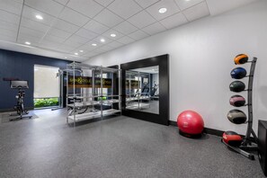 Uma academia com equipamentos de ginástica, uma bola de exercícios vermelha e um suporte de medicine ball fixado na parede.
