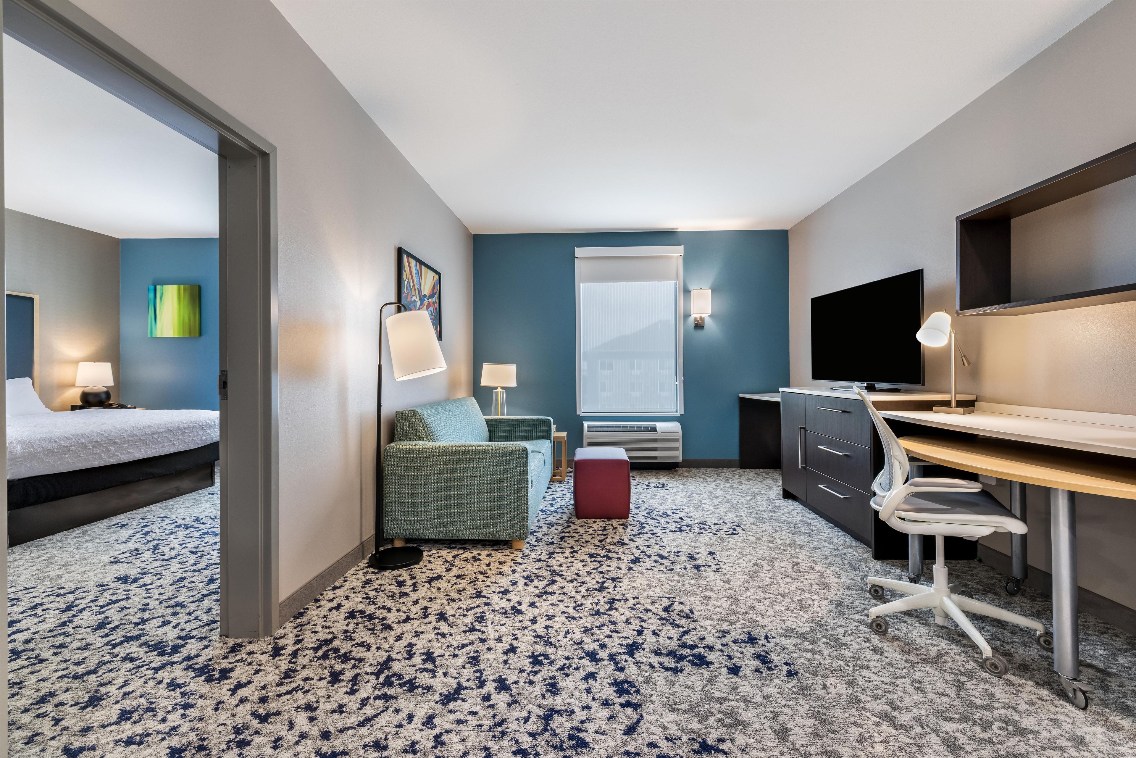 Habitación de hotel con cama, escritorio, silla, sofá, televisor y ventana.