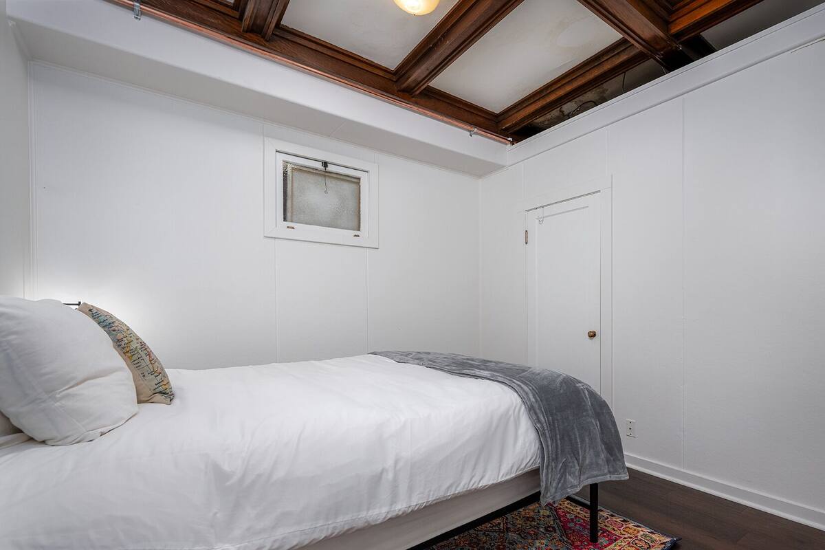 A bedroom with a bed, a window, a door, and a ceiling with wooden beams.