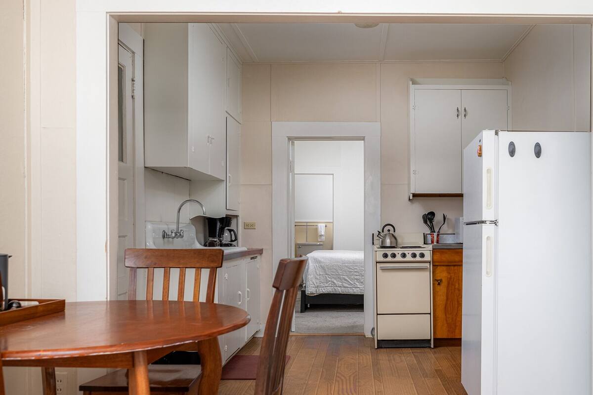 A compact kitchen with a dining table, a bed, and a refrigerator.