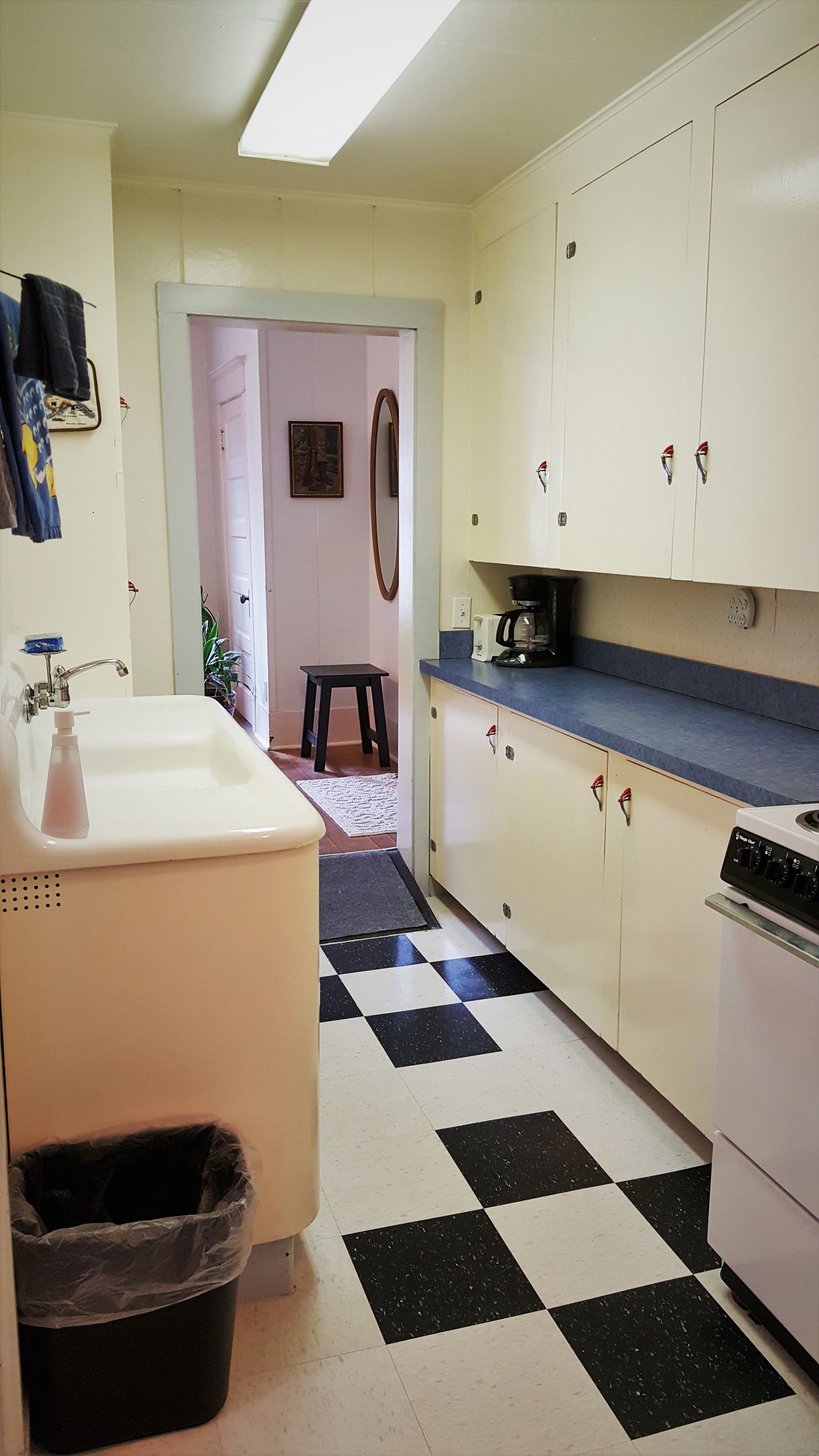 Una cocina con piso a cuadros, armarios blancos, un lavamanos y una cafetera.