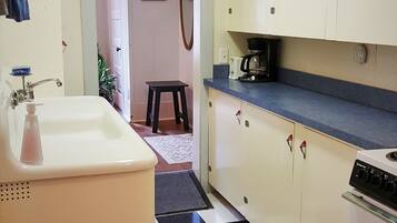 Una cocina con piso a cuadros, armarios blancos, un lavamanos y una cafetera.