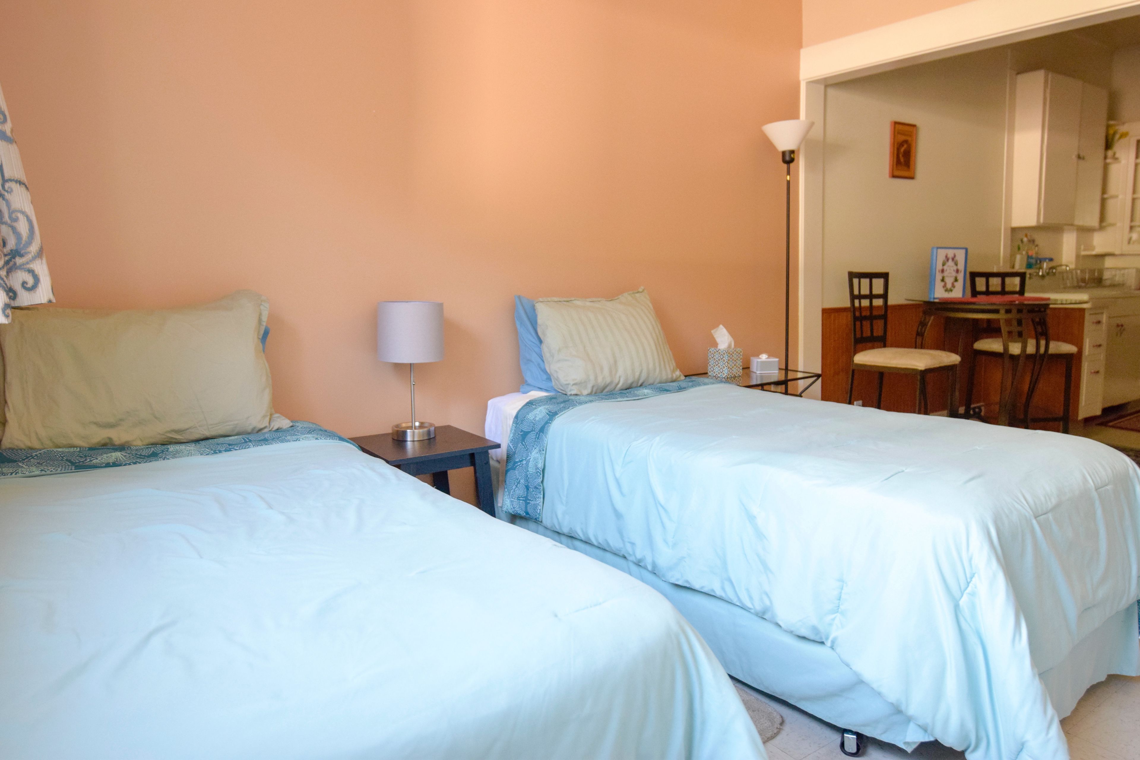 A bedroom with two beds, a nightstand, a lamp, and a small table with chairs.