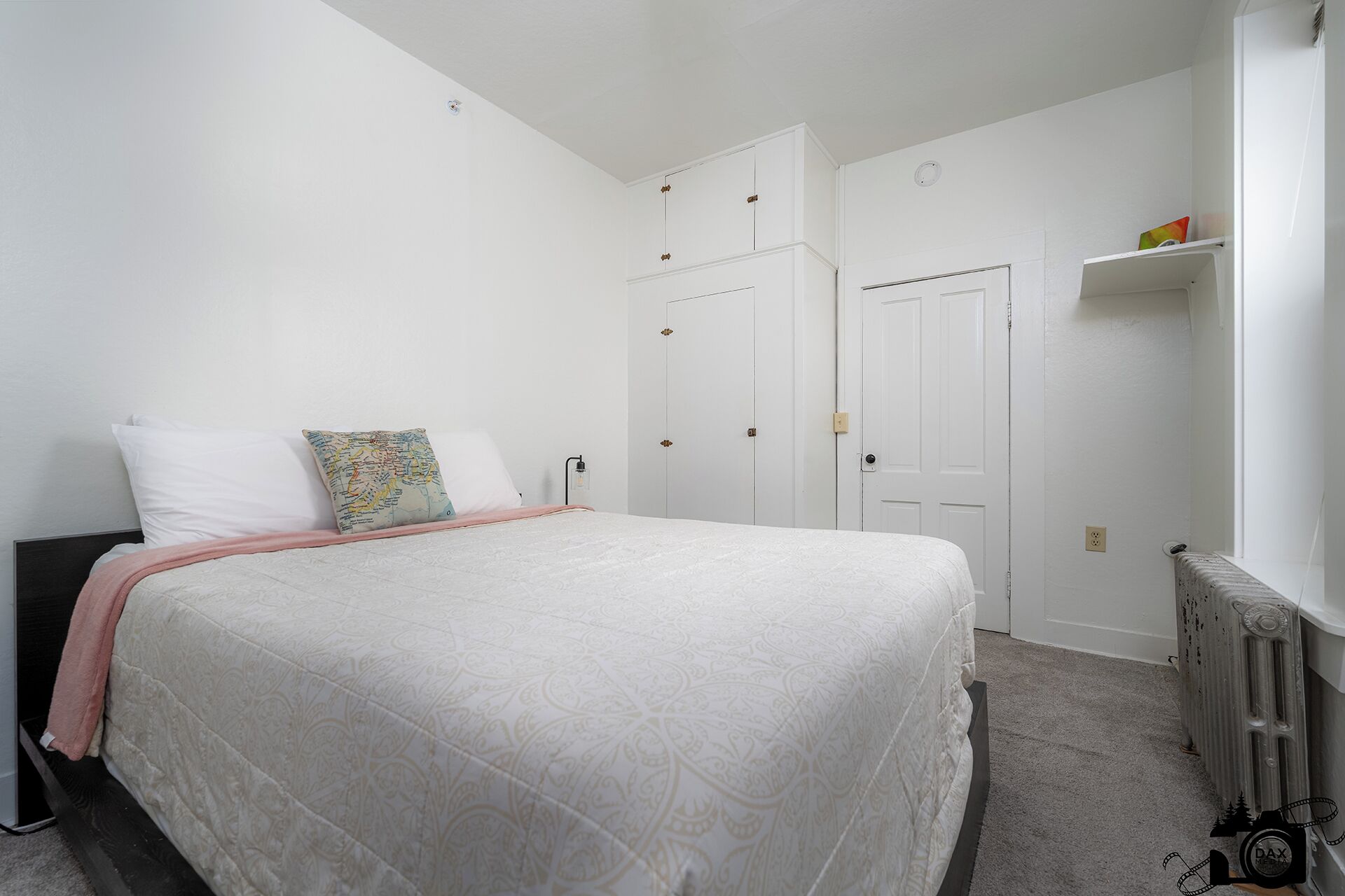 A bedroom with a large bed, white walls, a radiator, and a wardrobe.
