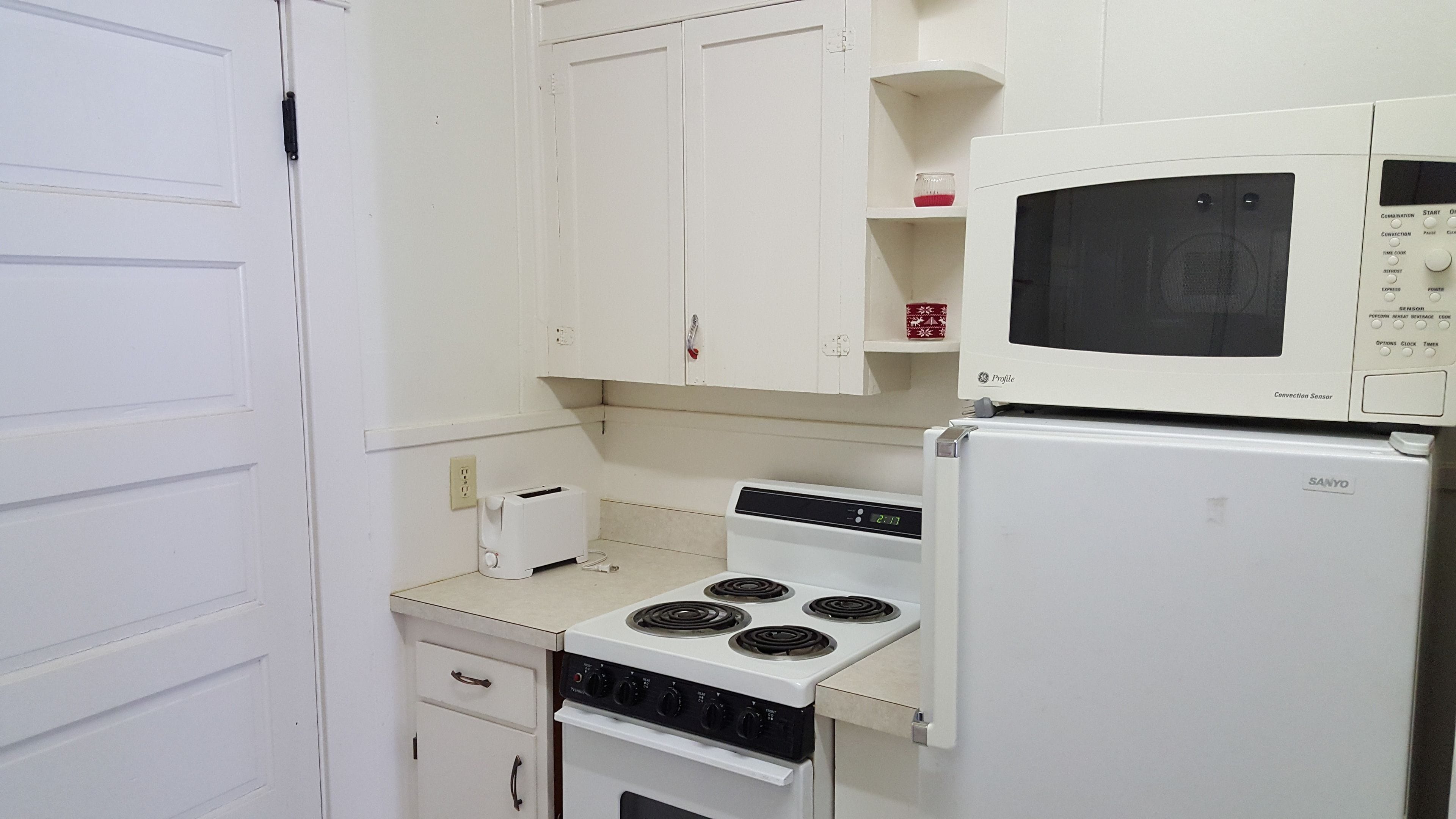 A compact kitchen with a white stove, a microwave, and a refrigerator.