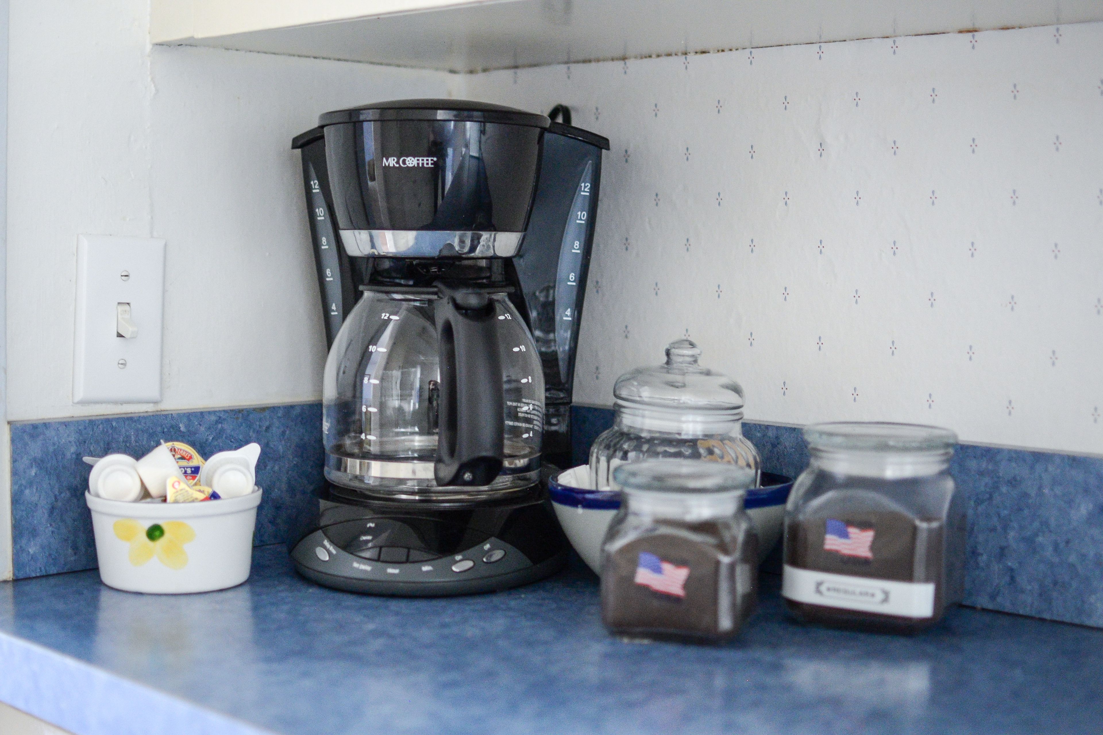 Uma cozinha com cafeteira, um recipiente com utensílios e dois potes de temperos.