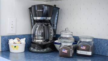Uma cozinha com cafeteira, um recipiente com utensílios e dois potes de temperos.