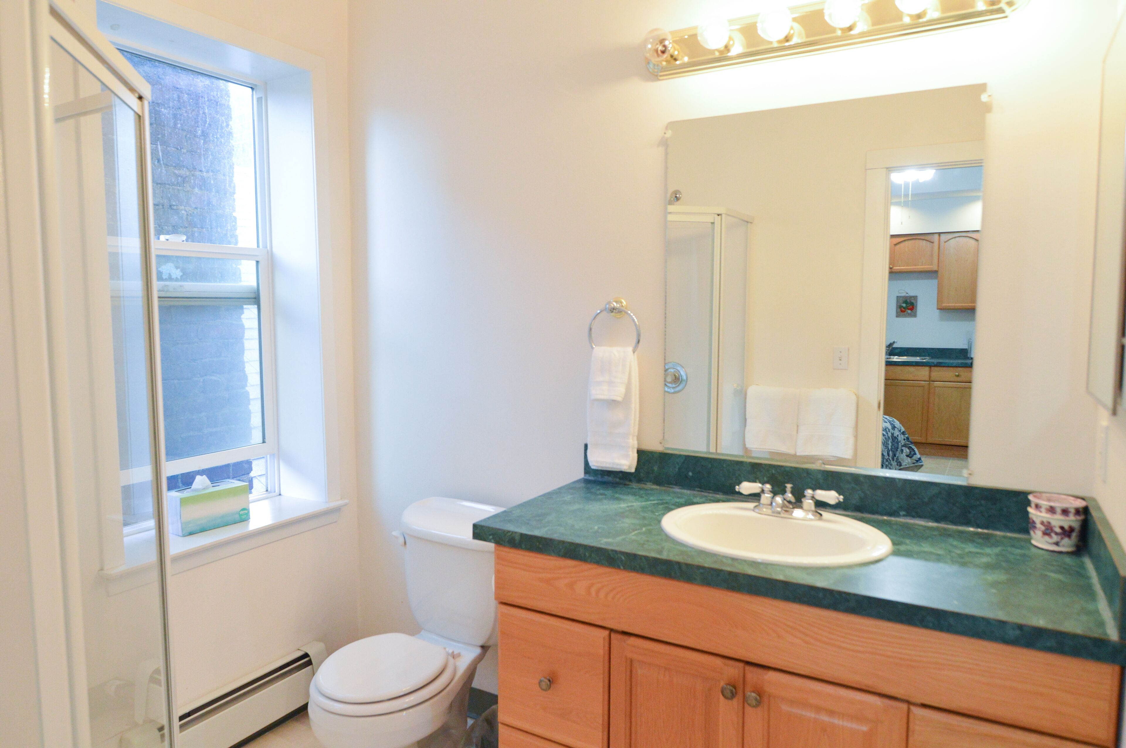 A bathroom with a toilet, sink, vanity, and a window.