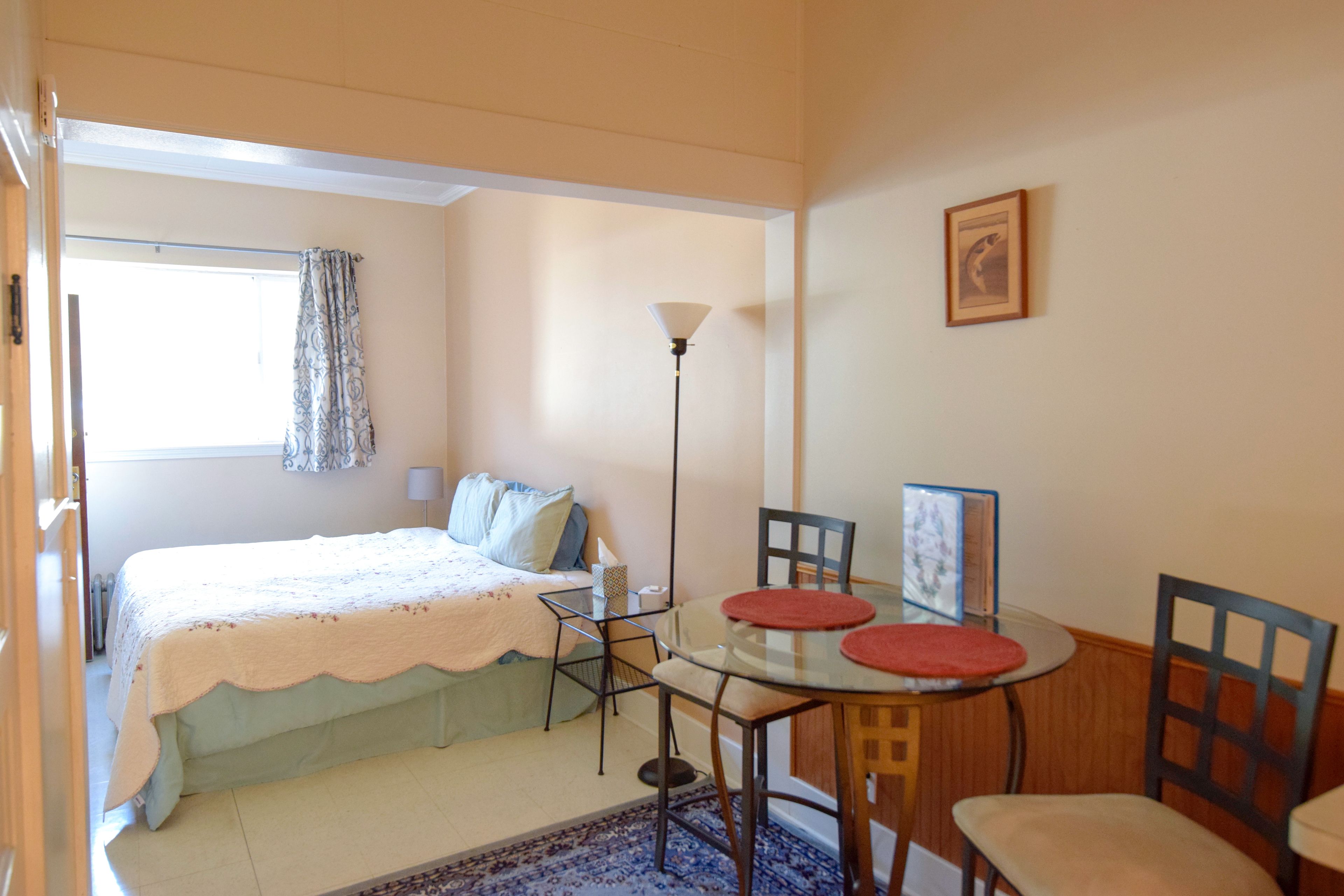 A bedroom with a bed, a bedside table, a lamp, and a window with curtains.