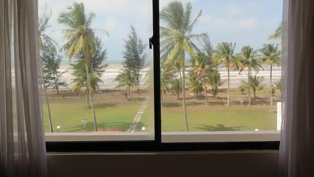 A room with a large window overlooking a beach with palm trees and a clear sky. - Seaview Hotel (Bandar Seri Begawan)
