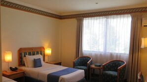 A hotel room with a bed, two armchairs, a small table, and a nightstand with a lamp and phone. - Seaview Hotel (Bandar Seri Begawan)