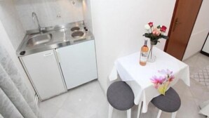 A compact kitchen with a sink, stove, and cabinets, a small table with a vase of flowers, and a door to the right. - Apartment Divna (Rovinj)