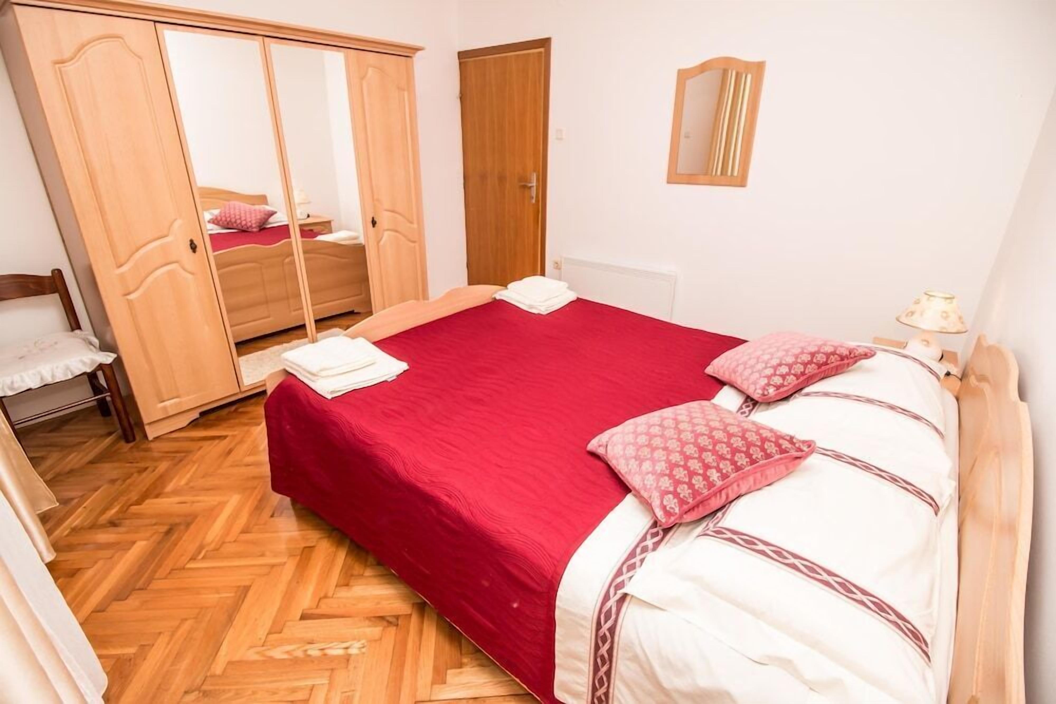 A bedroom with a large bed, wooden wardrobe, and a mirror on the wall.