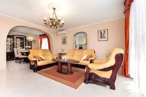 A living room with two leather sofas, a round coffee table, a chandelier, and a dining area in the background. - Apartment Divna (Rovinj)
