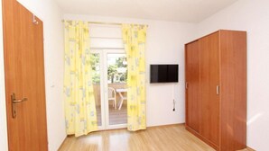 Una habitación con un armario de madera, un televisor montado en la pared y un ventanal corredero que da a una zona exterior con una mesa y sillas.