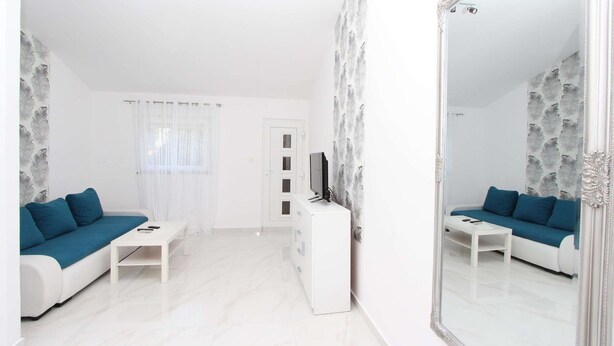 Una sala de estar moderna con un sofá blanco, un televisor sobre un mueble bajo y un espejo grande.
