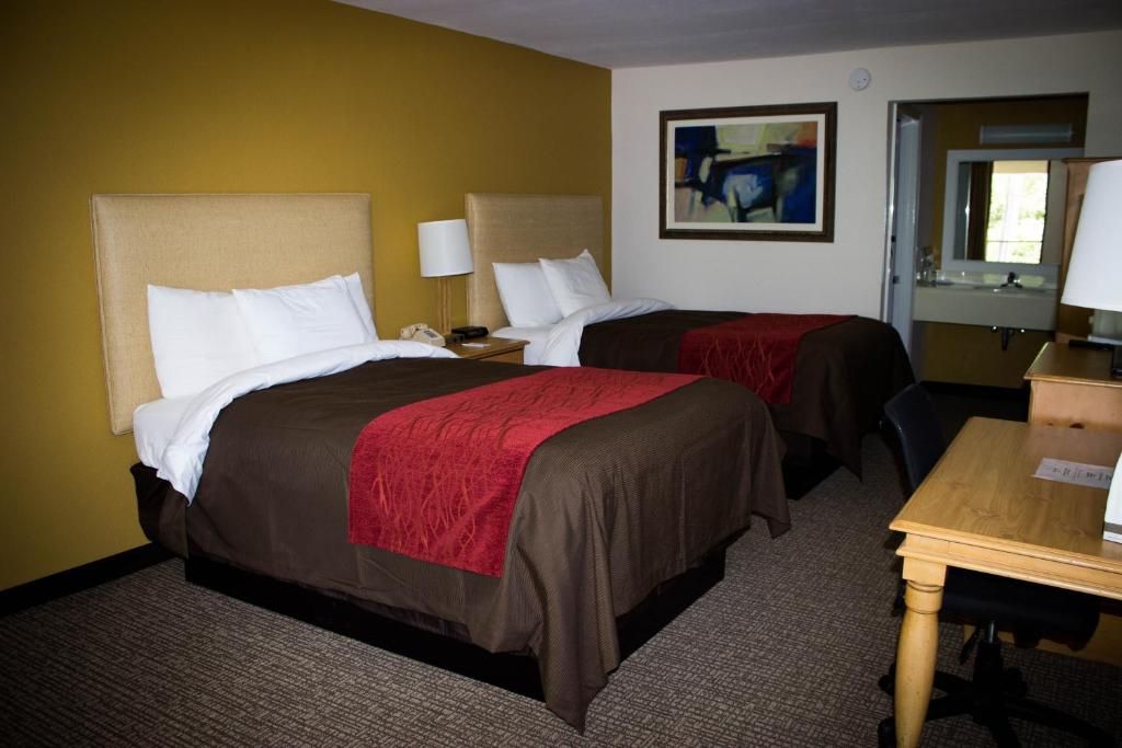 Quarto de hotel com duas camas, uma escrivaninha, uma cadeira, telefone e um quadro na parede.