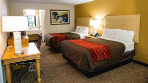 A hotel room with two beds, a desk with a lamp, a chair, and a painting on the wall. - Grand Vista Hotel (Helenwood)