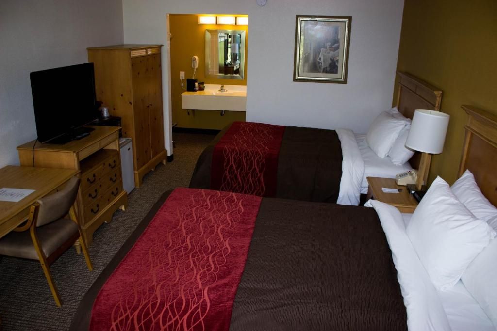 Ein Hotelzimmer mit zwei Betten, einem Schreibtisch, einem Fernseher, einem Kleiderschrank und einem Badezimmer mit Spiegel.