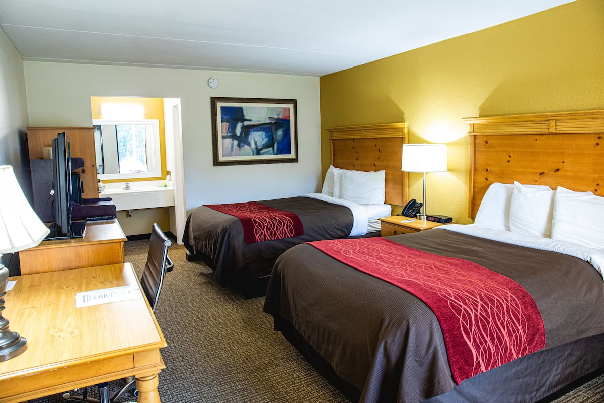 A hotel room with two beds, a desk, a chair, a television, and a painting on the wall.