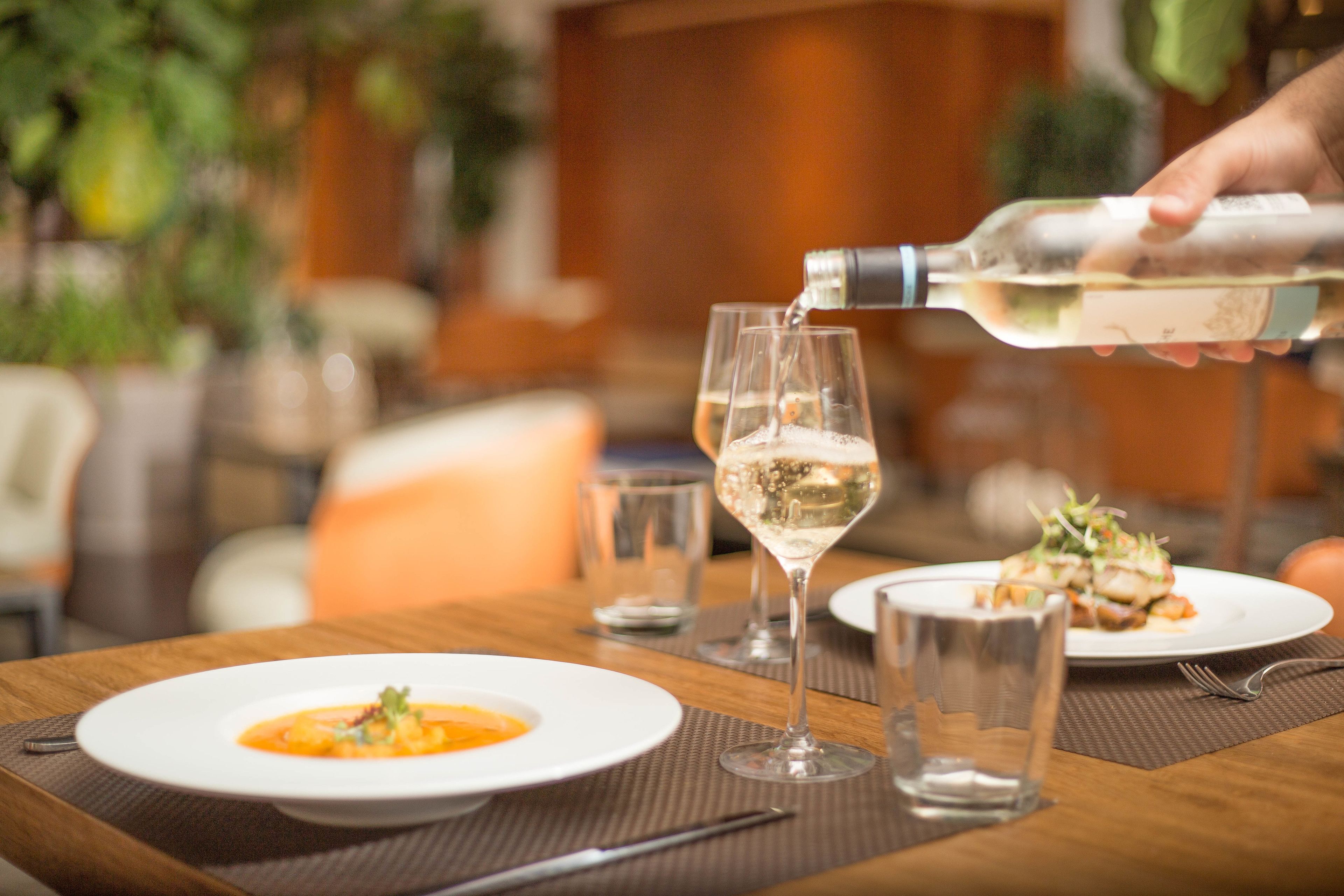 A dining table with plates of food, glasses, and a bottle being poured into a glass.