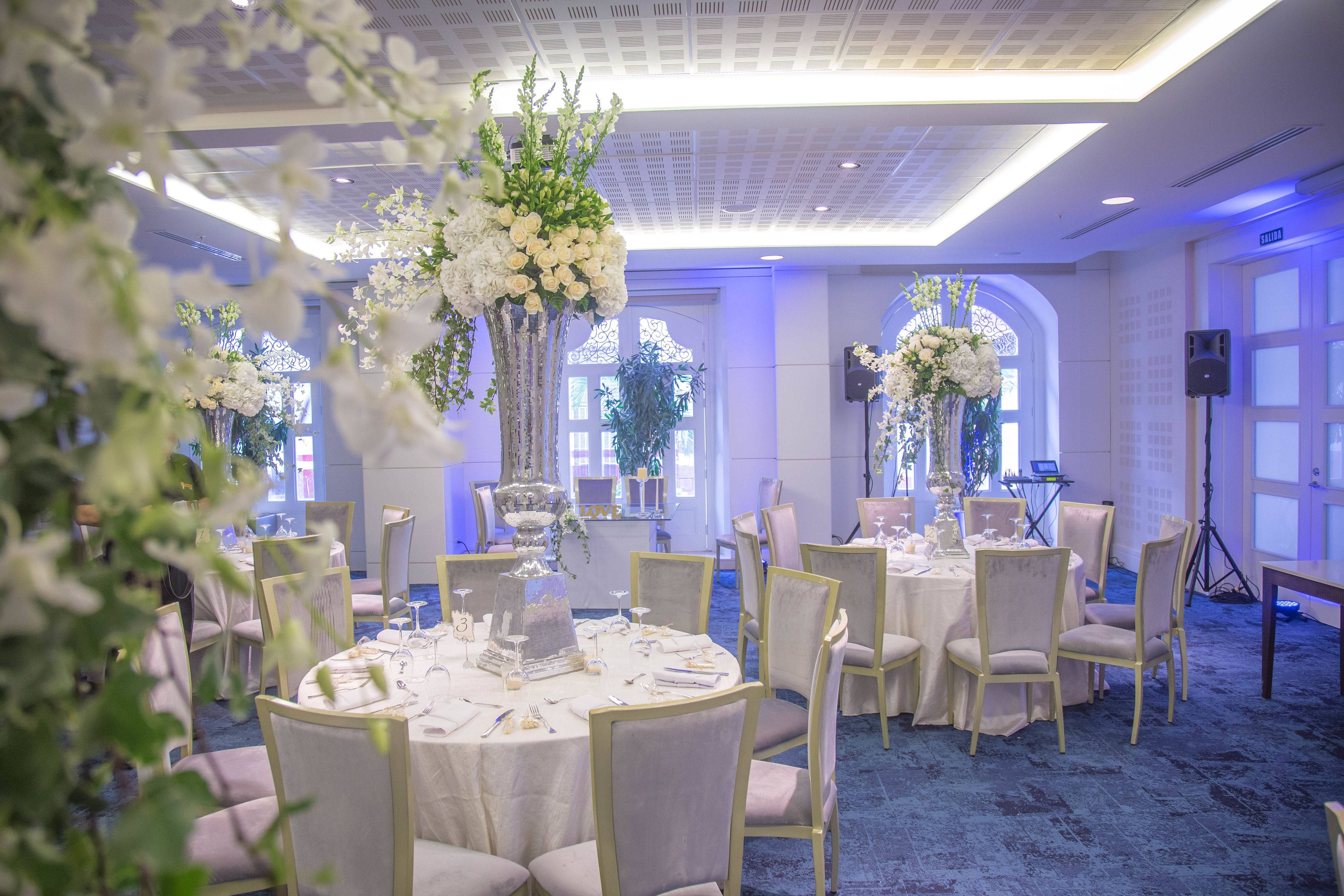A banquet hall with round tables, white tablecloths, and floral centerpieces.
