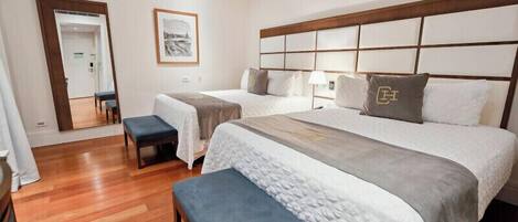 A hotel room with two beds, a bench, a mirror, and a framed picture on the wall.