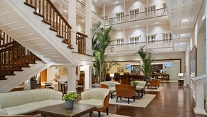 A spacious lobby with a wooden staircase, multiple seating areas, and a reception desk.