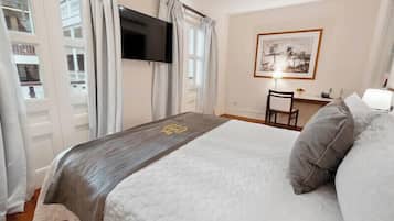 A hotel room with a bed, a desk with a chair, a flat-screen TV mounted on the wall, and a framed artwork above the desk.