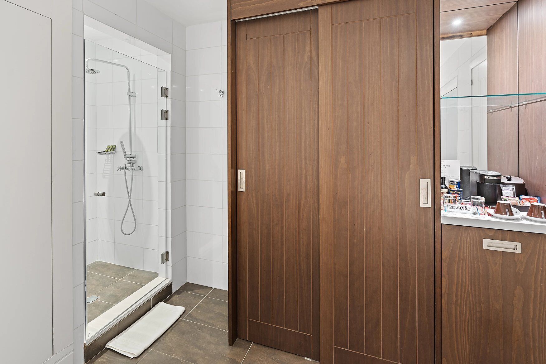 A modern bathroom with a glass-enclosed shower, wooden wardrobe, and a vanity with toiletries.