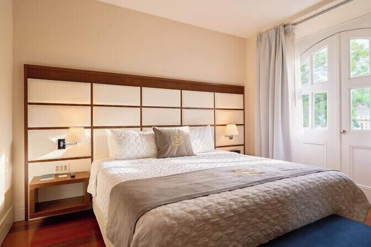 Une chambre d’hôtel avec un grand lit, une tête de lit composée de plusieurs panneaux, des lampes de chevet et un tableau encadré au mur.