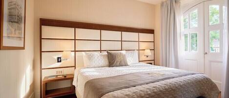A hotel room with a large bed, a headboard with multiple panels, bedside lamps, and a framed picture on the wall.
