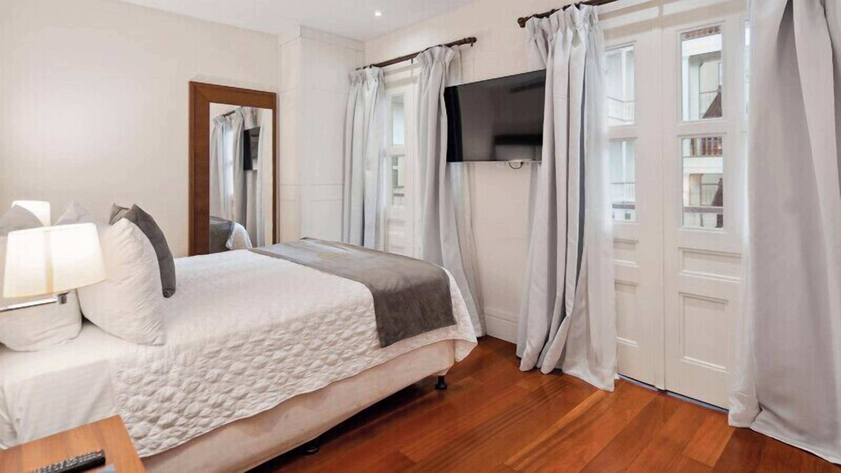 A bedroom with a bed, a TV mounted on the wall, and a window with curtains.