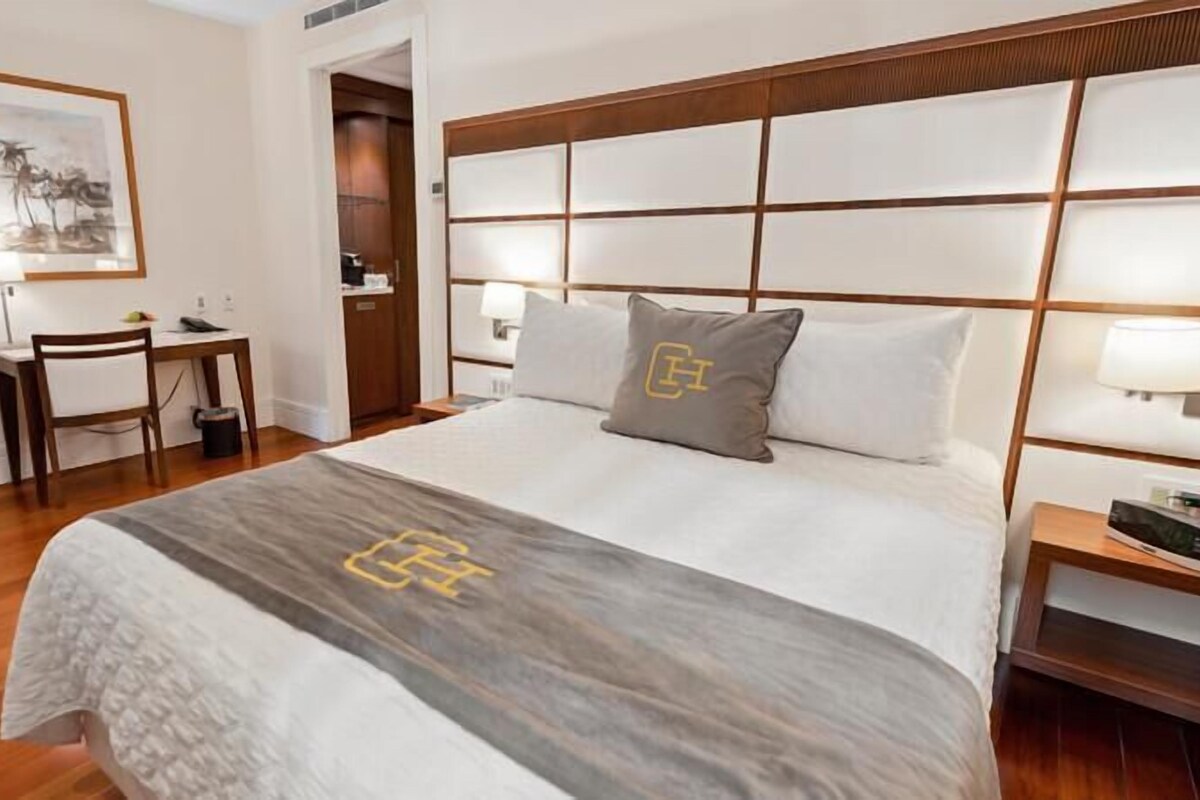 A hotel room with a large bed, a desk, a chair, and a framed picture on the wall.