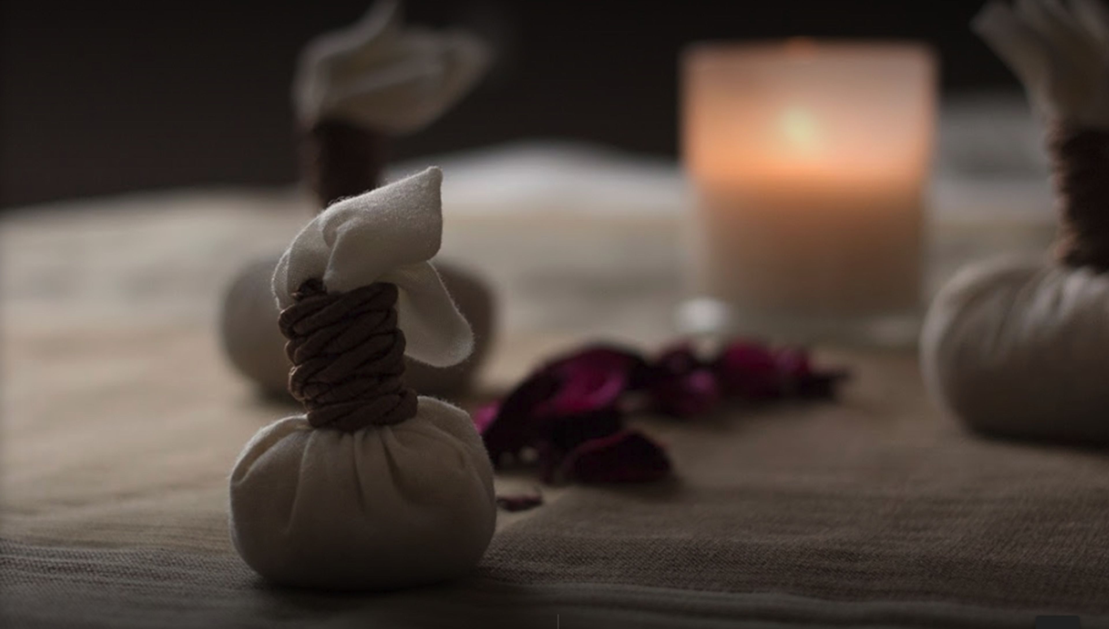 A candle, a small white object, and scattered rose petals on a table.