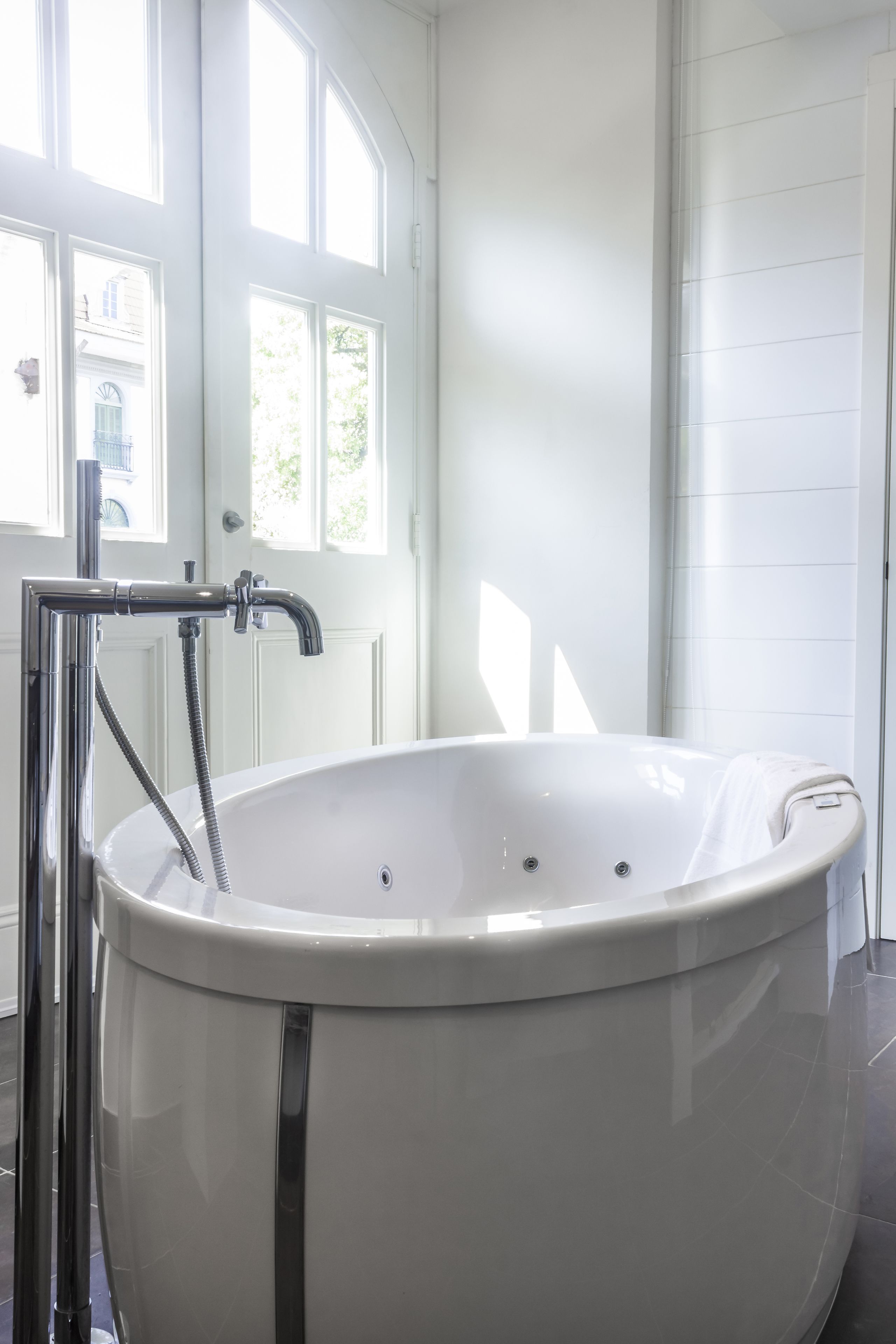 A modern bathroom with a freestanding bathtub, a chrome showerhead, and a white door with windows.