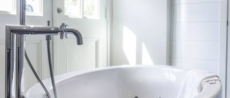 A modern bathroom with a freestanding bathtub, a chrome showerhead, and a white door with windows.