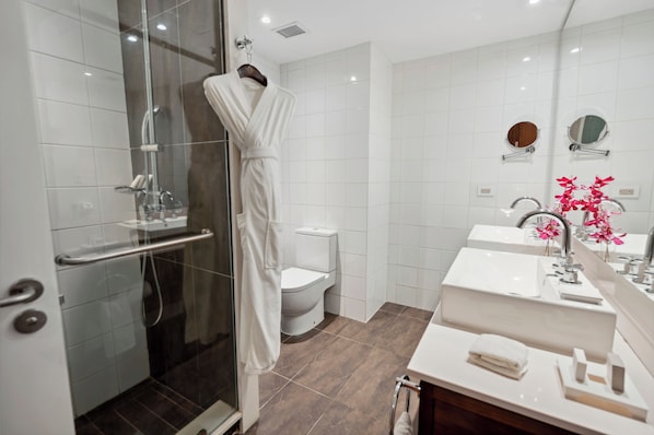 Un baño moderno con ducha de vidrio, inodoro blanco y tocador con dos lavabos y un espejo.