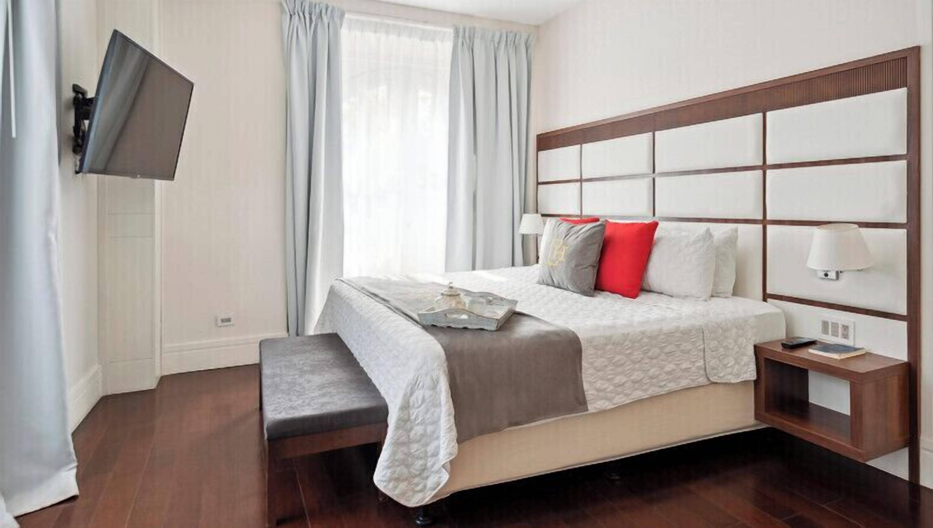 A neatly arranged hotel room with a large bed, a bedside table with a lamp, and a flat-screen TV mounted on the wall.