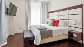 Habitación de hotel ordenada con una cama grande, una mesita de noche con lámpara y un televisor de pantalla plana montado en la pared.