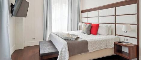 A neatly arranged hotel room with a large bed, a bedside table with a lamp, and a flat-screen TV mounted on the wall.