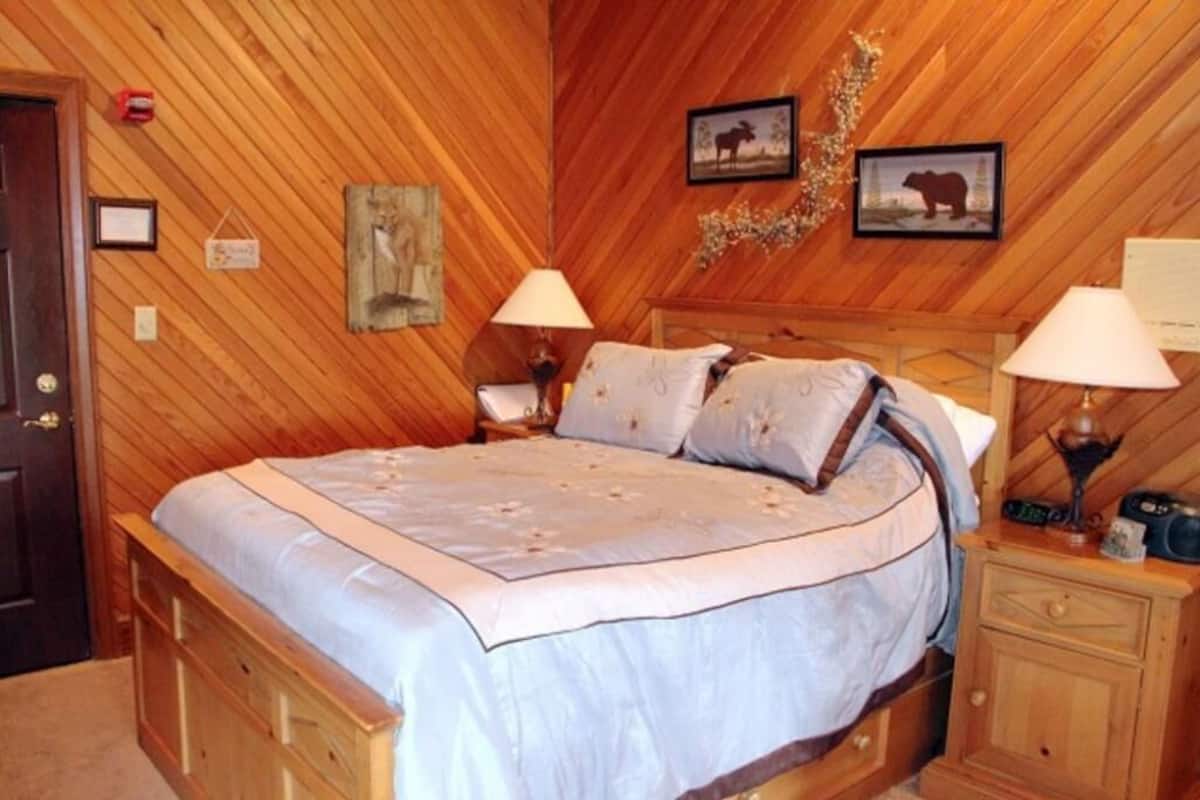 A wooden-paneled bedroom with a bed, two bedside lamps, and framed pictures on the wall.